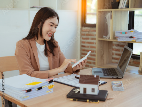 Photography A real estate agent or manager sits at a desk in a modern office, working on a laptop with miniature house models