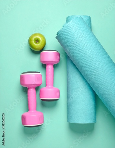 Yoga mat, exercise weights and a green apple on pastel background. 
