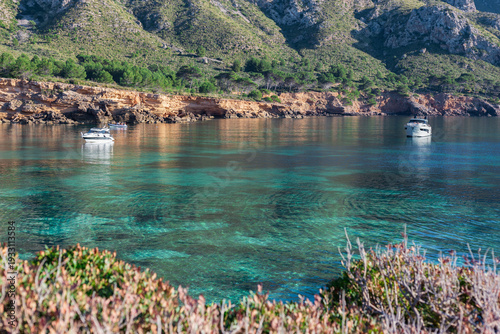 Beautiful cove at Playa Es Calo in Mallorca with anchored boats clear water and mountains in background