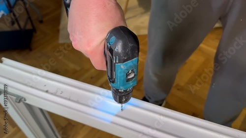 Close view of hands using cordless drill on white metal frame, home renovation and diy assembly task, practical workshop mood for maintenance and repair use