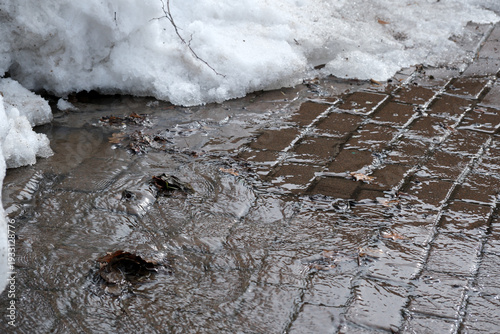 Snow melting and puddles forming on a cobblestone sidewalk in spring
