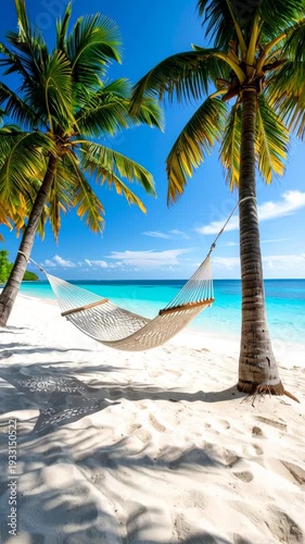 Relaxing white hammock hanging between two palm trees on a tropical beach with turquoise ocean water