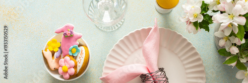 A vibrant Easter table setting features a beautifully arranged plate with a wrapped egg, decorated cookies, and fresh flowers, creating a joyful atmosphere for the holiday gathering, banner