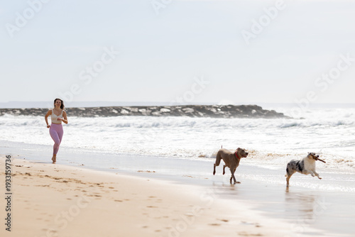 Fényképezés Woman running with dogs on sandy beach