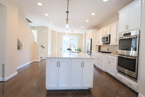 Empty home kitchen interior featuring white cabinets, large stone island, wood floors, and stainless steel appliances