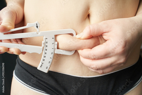 Adult caucasian female measuring body fat with caliper health, fitness, and self-assessment concept.