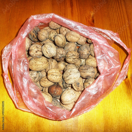Fresh whole walnuts in a red plastic bag on a wooden table