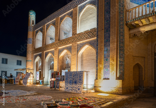 Khiva, Khorezm Province, Uzbekistan - May 30, 2025: Night View of Illuminated Historic Architecture and Traditional Suzani Textiles Market in the Ancient City of Khiva