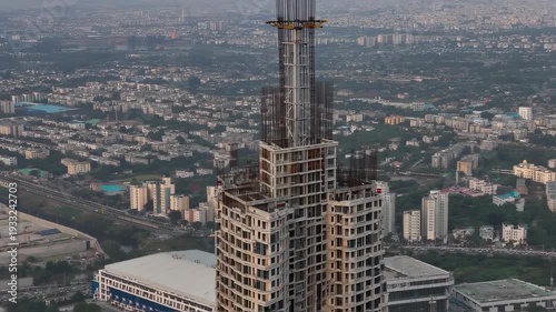 Cityscape with rising skyscraper. Skyline snapshot showing underconstruction tower and busy metropolis. Aerial perspective of emergent skyscraper amidst sprawling urban environment at dusk
