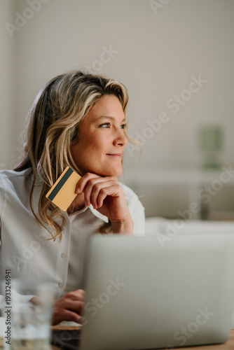 Wallpaper Mural Woman using a credit card and laptop for online shopping, contemplating her next purchase or financial decision Torontodigital.ca