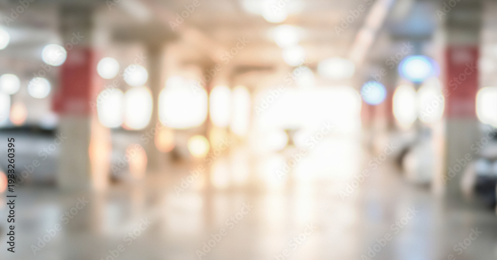 Obraz premium Blurred view of an indoor parking garage with bright lights and white vehicles visible in the background. The overall atmosphere is spacious and modern.