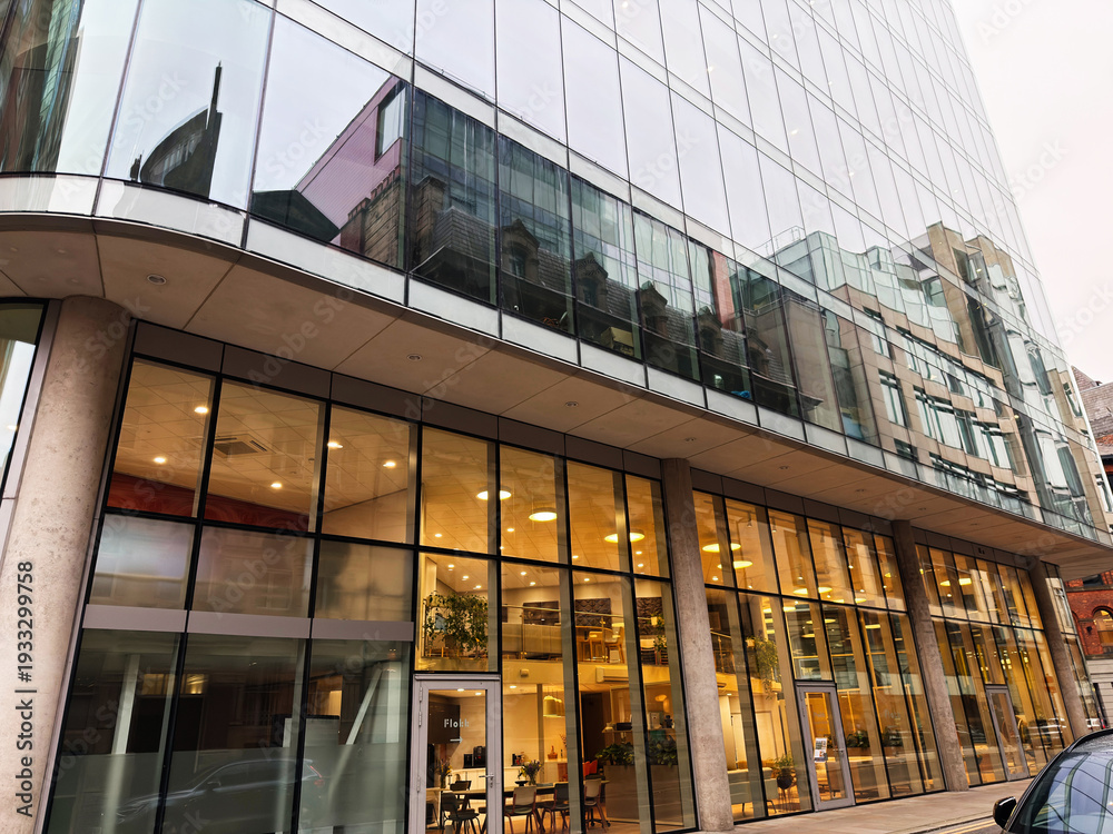 Obraz premium Modern glass office building in Manchester, UK, with glass facade and warm The Flokk showroom interior lighting visible