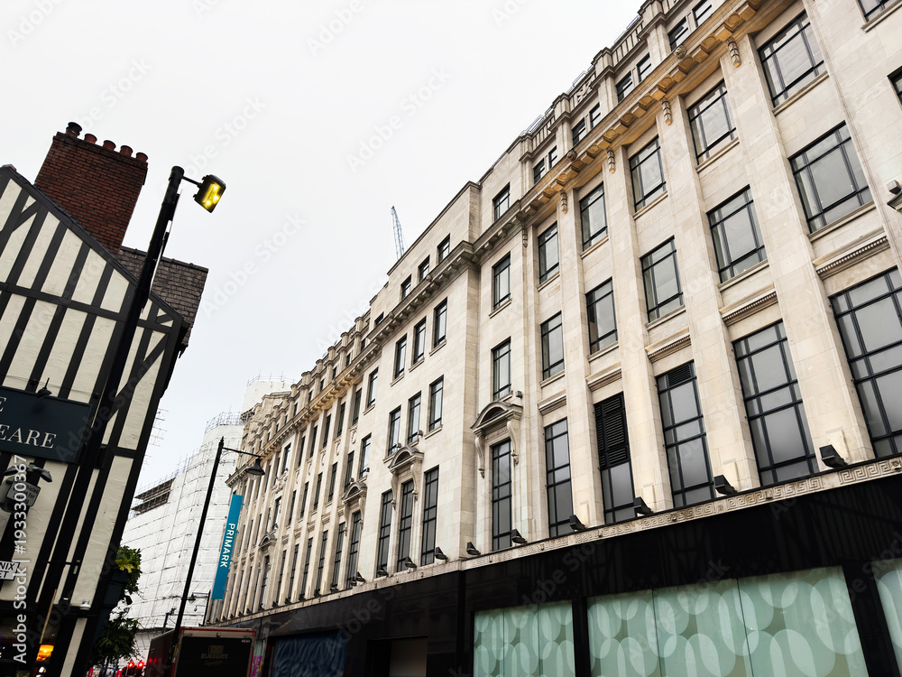 Fototapeta premium Historic street in Manchester with tall windows, modern storefronts, and a street lamp, grand architecture