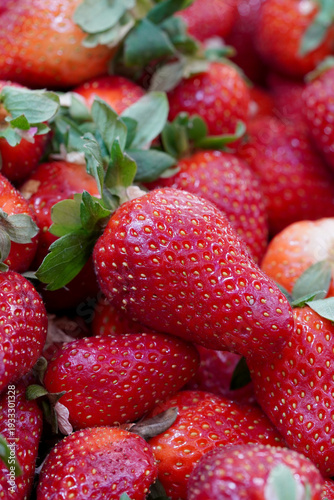 Extreme close-up of fresh ripe red strawberries with green leaves, highlighting the detailed seed texture and vibrant organic fruit surface
