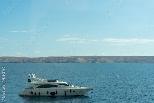 Luxury white motor yacht anchored in calm blue Adriatic Sea with barren island coastline on horizon under clear summer sky. Concept of wealth, luxury lifestyle and exclusive sea vacation.