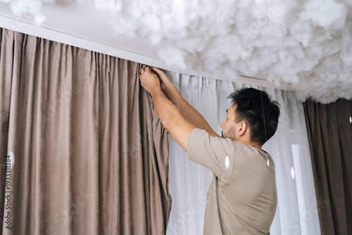 Photos Shooting from below of man hanging curtains on modern curtain rail, installing n