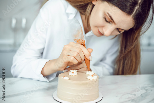 Confectioner decorates cake with icing in a kitchen setting during daylight hours