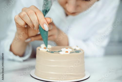 Confectioner decorates cake with icing in a kitchen setting during daylight hours
