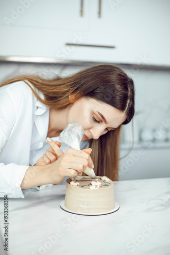 Confectioner decorates cake with icing in a kitchen setting during daylight hours