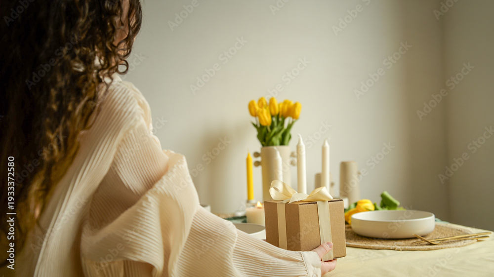 Fototapeta premium Woman holding a gift box with a ribbon on a table with tulips and candles