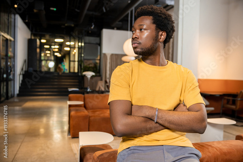 Foto African American man sitting on sofa with arms crossed looking away in coworking