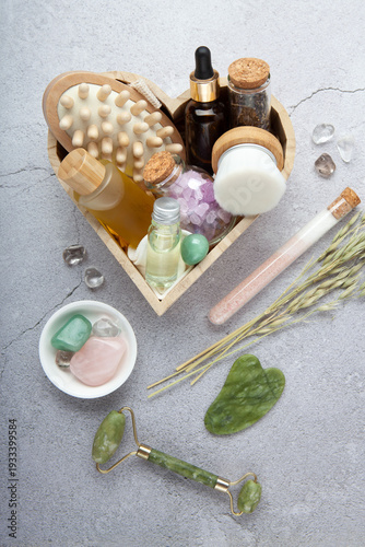 Holiday gift set for home spa with green jade roller, gua sha, facial oil, amber bottle, eco friendly packaging on gray stone background