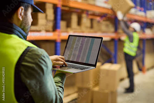 Tableau sur toile Warehouse inventory worker with laptop near shelves