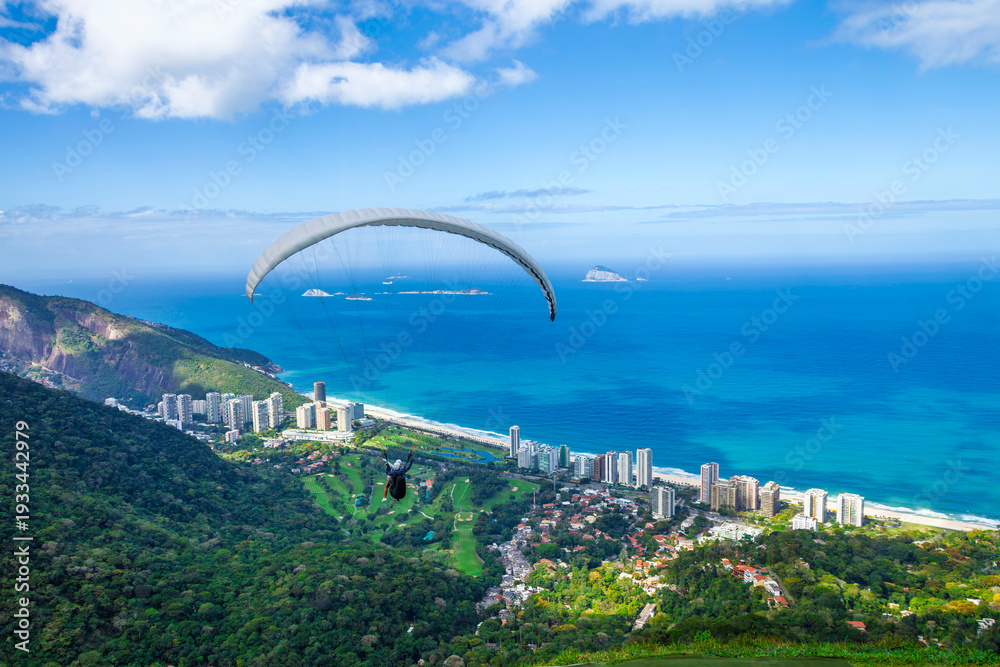 Fototapeta premium Paraglider soaring over the Atlantic Ocean and São Conrado beach with a view of the green mountains and luxury buildings in Rio de Janeiro, Brazil.