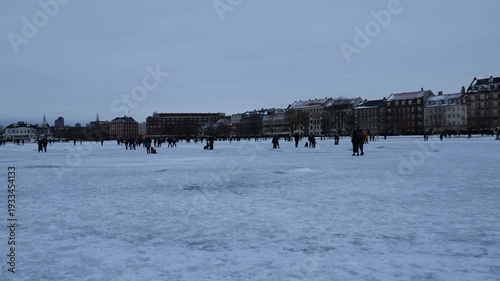 A winter landscape of Copenhagen, Denmark. The photograph depicts a wide, snow-covered square, or frozen urban space, in the center of the capital, where people stroll on a cold winter day