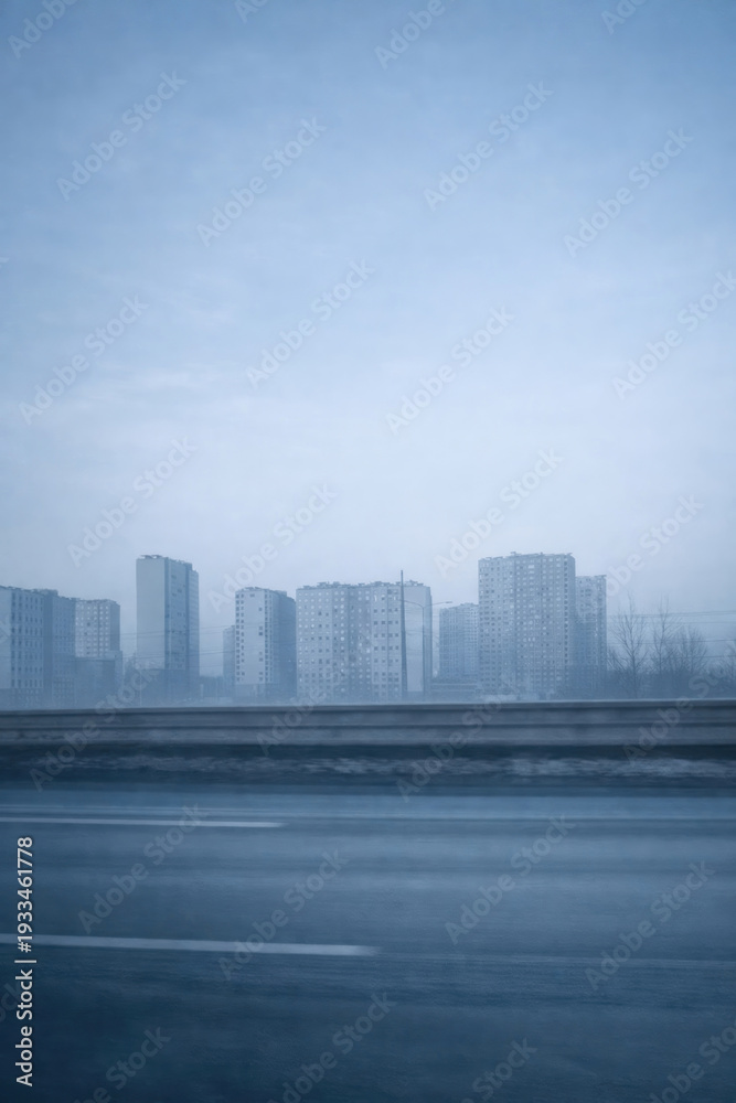 Fototapeta premium A foggy cityscape with silhouettes of multi-story residential buildings against a cold blue sky. 