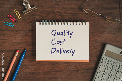 Corporate and management concept of Quality Cost Delivery represented on notebook with pen, clips, glasses. Professional business leadership and operations.