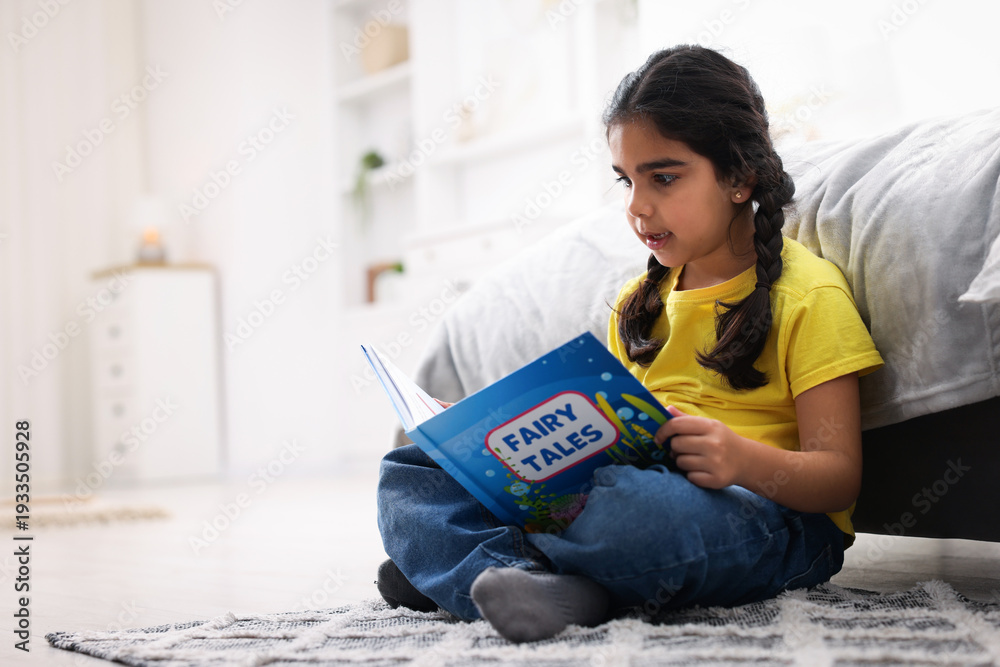 Naklejka premium Cute little girl reading book on floor at home. Space for text