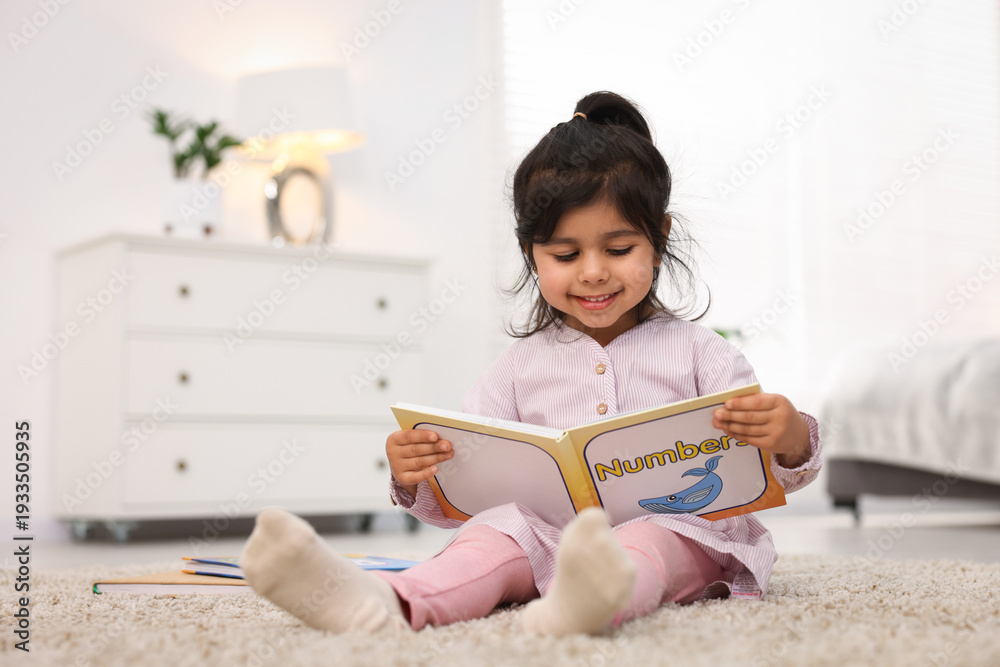 Naklejka premium Cute little girl reading book on floor at home. Space for text