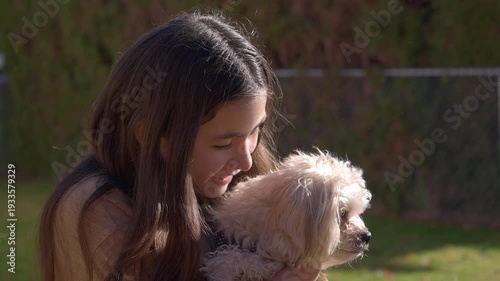 Child with her white fluffy small dog, holding and petting the dog. Dog turns and looks at the camera and the young girl.
