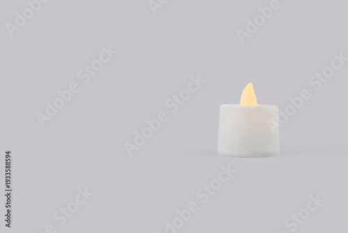Small LED candle with warm glowing flame isolated on white background. Minimalist photography with copy space, flameless electric candle symbolizing peace, relaxation, home decor, mindfulness 