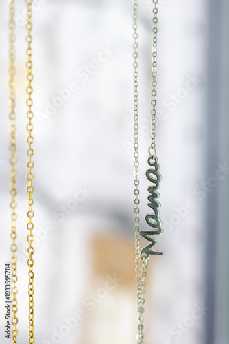 Jewelry shop display shows silver and gold chains with word necklace on chain during daytime