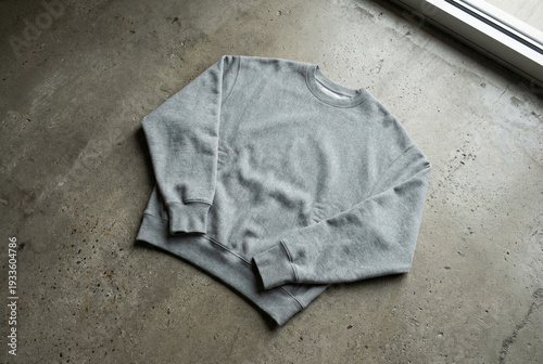 A plain grey crewneck sweatshirt lying flat on a textured concrete floor.