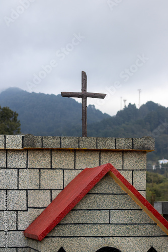 Cross stands on top of a building with mountains in the background during anovercast day