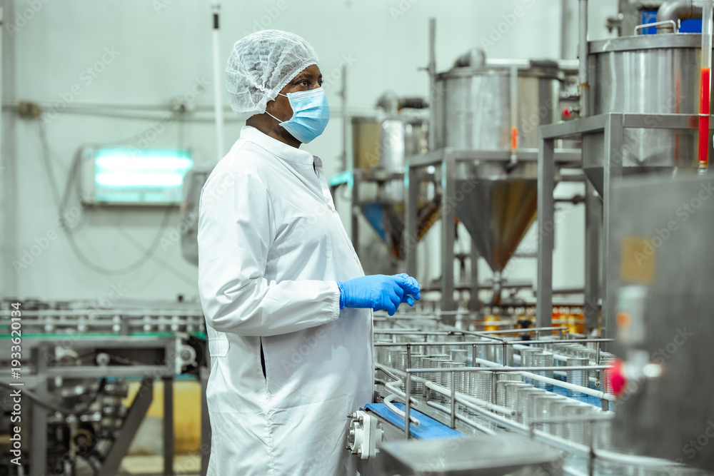 Naklejka premium Food safety supervisor observes canned seafood production line monitors empty metal containers on conveyor system inside processing plant, HACCP compliance contamination prevention standards.