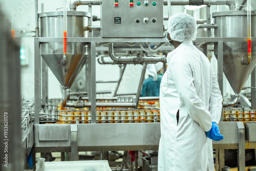 Industrial technician inspects processing equipment and oversees canned food filling system inside seafood factory, representing automation workflow and food safety management standards.
