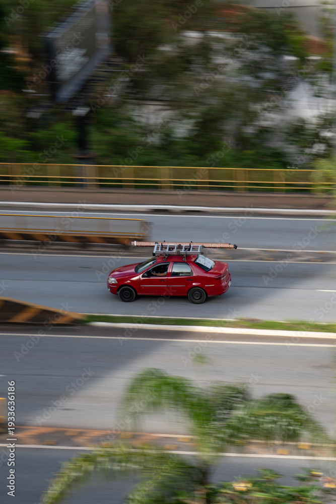Fototapeta premium Red Fiat Siena side profile in motion, Compact work sedan driving on city avenue