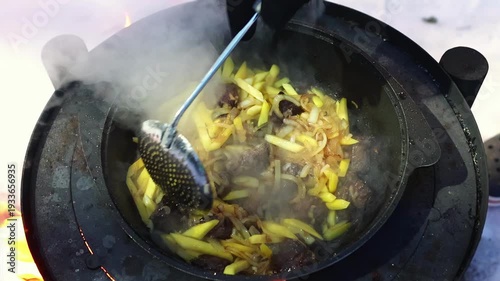 Steam rising from frying pan with beef meat and potato, carrot placed on metal stove outdoors. Wilderness cuisine concept, expedition lifestyle and seasonal mood.