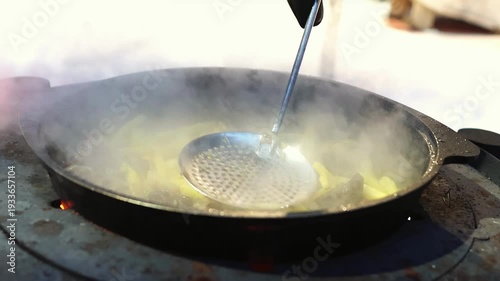 Hot meal simmering above wood burning fire in cold environment. Outdoor adventure cooking and cozy warmth atmosphere. Fried potato and beef meat stirring in steaming pan.