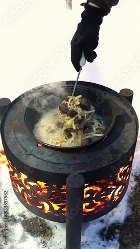 Steam rising from pan on portable stove during cold season. Outdoor food preparation, expedition lifestyle and survival theme. Man stirring pilaf in hot pan outdoor, vertical shot.