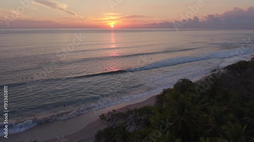 Forward aerial movement over palm trees toward glowing tropical sunset and ocean waves