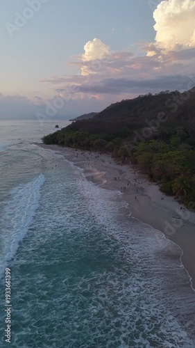 Vertical aerial glide following ocean waves along tropical beach coastline at sunset