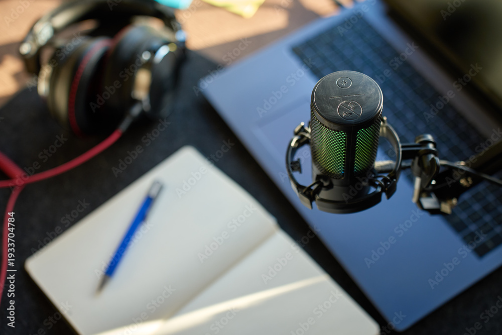 Fototapeta premium Close up of podcast microphone above laptop, headphones, and notebook on desk. Concept of recording, streaming and content creation