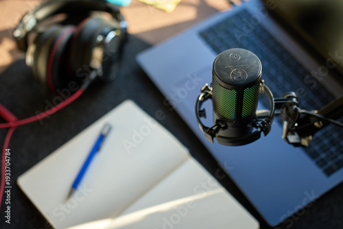 Close up of podcast microphone above laptop, headphones, and notebook on desk. Concept of recording, streaming and content creation