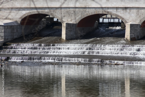 Urban drainage cascade with stepped weir. Excess stormwater flows from upper pond to lower basin creating small waterfalls under bridge
