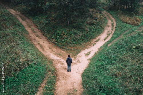 A person stands at a crossroads, two dirt paths diverging in a forest setting